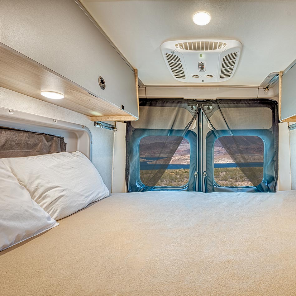 The rear bed made up with white linen, looking through the back doors to a mountain lake